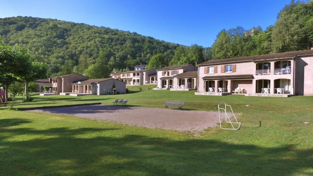 A row of single-story buildings with balconies, a grassy lawn, and a hilly backdrop.