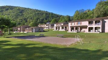 A row of single-story buildings with balconies, a grassy lawn, and a hilly backdrop.