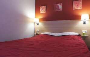 Habitació d'hotel amb una llitera vermella, dues làmpades al costat del llit i tres quadres a la paret.