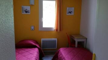 Een kamer met twee bedden, een raam met gordijnen, een radiator en een klein tafeltje.