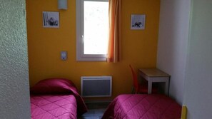 Een kamer met twee bedden, een raam met gordijnen, een radiator en een klein tafeltje.