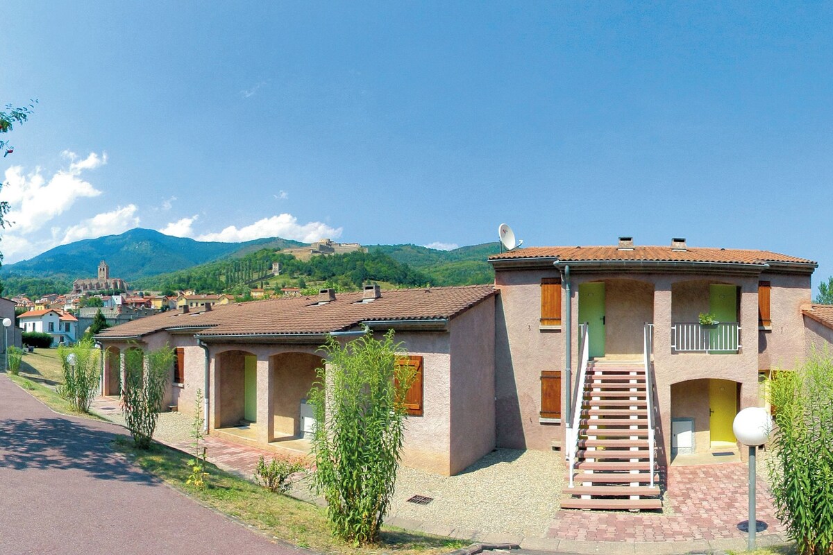 Une rangée de bâtiments de style méditerranéen traditionnel, avec des toits en tuiles de terre cuite, un escalier central et une chaîne de montagnes en arrière-plan.