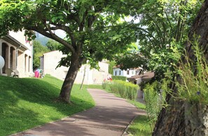 A paved path flanked by lush greenery and traditional buildings with arched windows. - Vvf Villages Prats de Mollo (Serralongue)