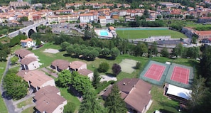 Vue aérienne d’un quartier résidentiel avec des maisons, une piscine, des courts de tennis et un pont.