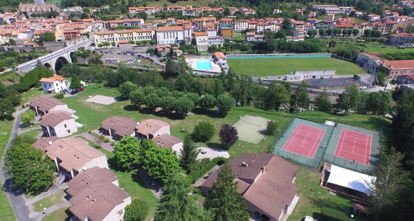 Luchtbeeld van een woongebied met huizen, een zwembad, tennisbanen en een brug.