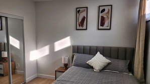 A bedroom with a bed, a nightstand, a lamp, and two abstract paintings on the wall. - Deluxe 2-BR Basement Suite in South East Calgary (Calgary)