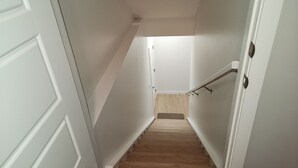 A narrow hallway with white walls and a wooden staircase leading to a landing. - Deluxe 2-BR Basement Suite in South East Calgary (Calgary)