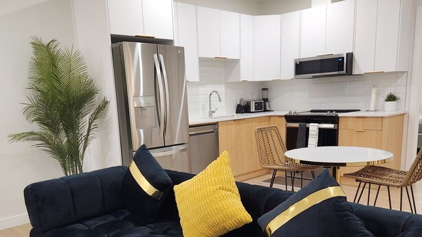 A modern living room with a dark blue sofa, yellow cushions, and a white rug. - Deluxe 2-BR Basement Suite in South East Calgary (Calgary)