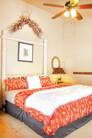 A bedroom with a bed, a ceiling fan, a framed picture, a lamp, and a mirror. - EML 9 Juniper (Paonia)