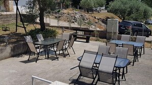 Un patio al aire libre con varias mesas y sillas, un muro de piedra y un coche estacionado al fondo.