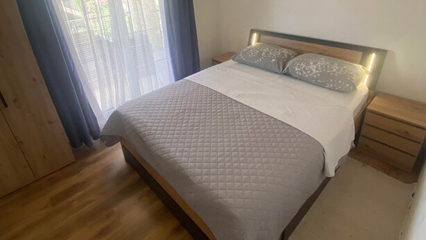 Un dormitorio con cama, suelo de madera, una mesita de noche y una ventana con persianas.