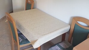 Una mesa de comedor con mantel estampado, dos sillas de madera con cojines verdes y una puerta blanca con manija.
