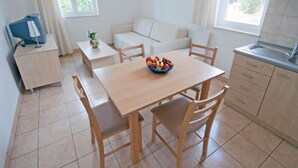 Een lichte, moderne woonkamer met een houten eettafel, twee banken, een kleine televisie en een keuken met een spoelbak en kastjes.