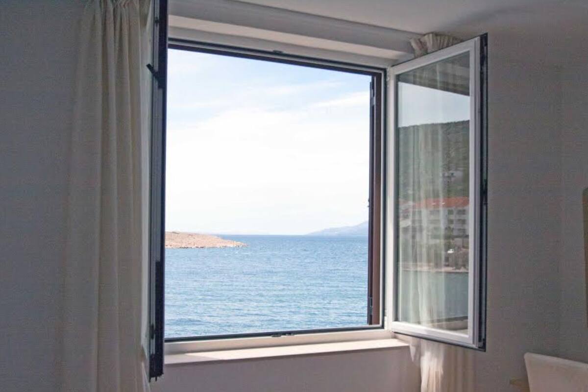 A room with a large window offering a view of the sea and a distant landmass.