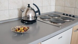 Een keuken met een fornuis, waterkoker en een schaal met fruit op het aanrecht.