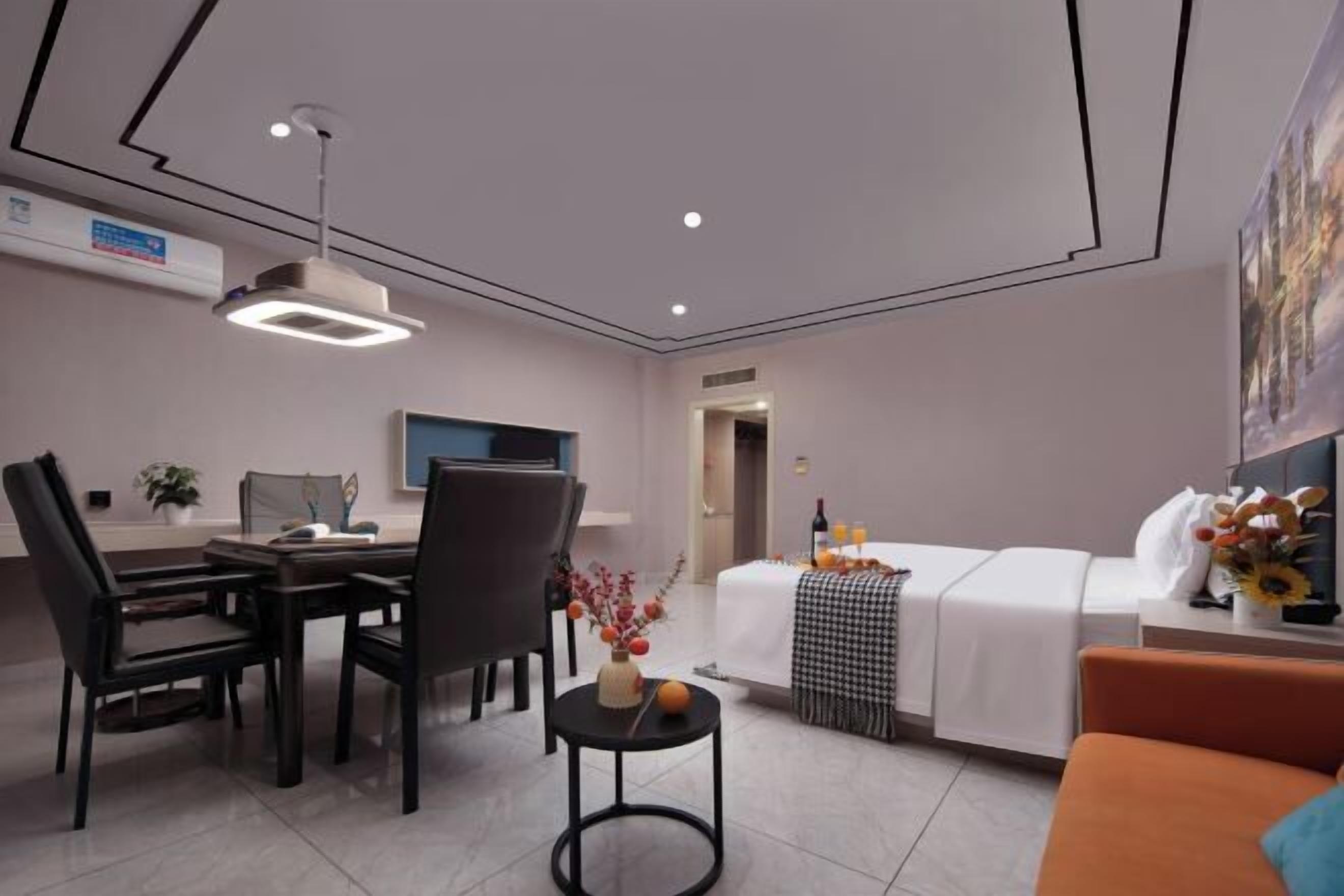 A modern hotel room with a dining area, a bed with a checkered blanket, a small table with a vase, and a sofa.