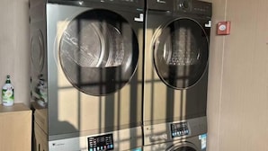 A wall-mounted, stainless steel, front-loading washer and dryer unit with a control panel and a small red tag on the wall. - Yunfu Jinyu Hotel (Yunfu Bus Station Yihua International Plaza) (Yunfu)