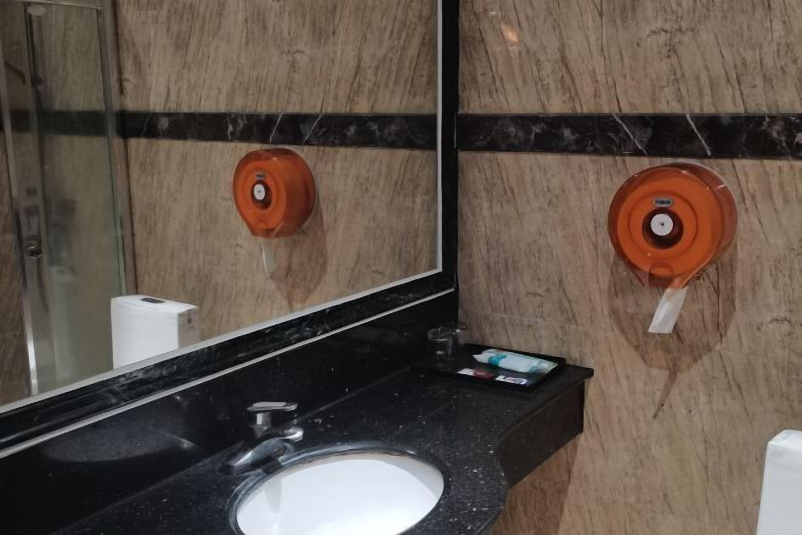 A bathroom with a black countertop, a white sink, and a mirror. There are two soap dispensers on the wall.