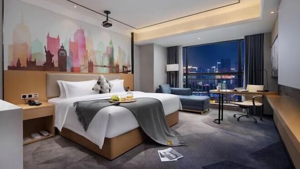 A modern hotel room with a large bed, a desk, and a view of the city skyline at night. - Yunfu Jinyu Hotel (Yunfu Bus Station Yihua International Plaza) (Yunfu)