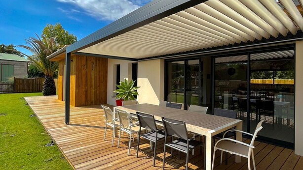 Un espace de restauration extérieur moderne, doté d’une terrasse en bois, d’un patio couvert et offrant une vue sur l’immeuble voisin.