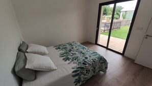 Une chambre à coucher avec un lit, des oreillers et une vue sur un jardin à travers une porte-fenêtre coulissante.