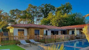Une zone avec une piscine, délimitée par une clôture en bois, un petit bâtiment avec un toit recouvert de tuiles rouges, et un palmier au premier plan.