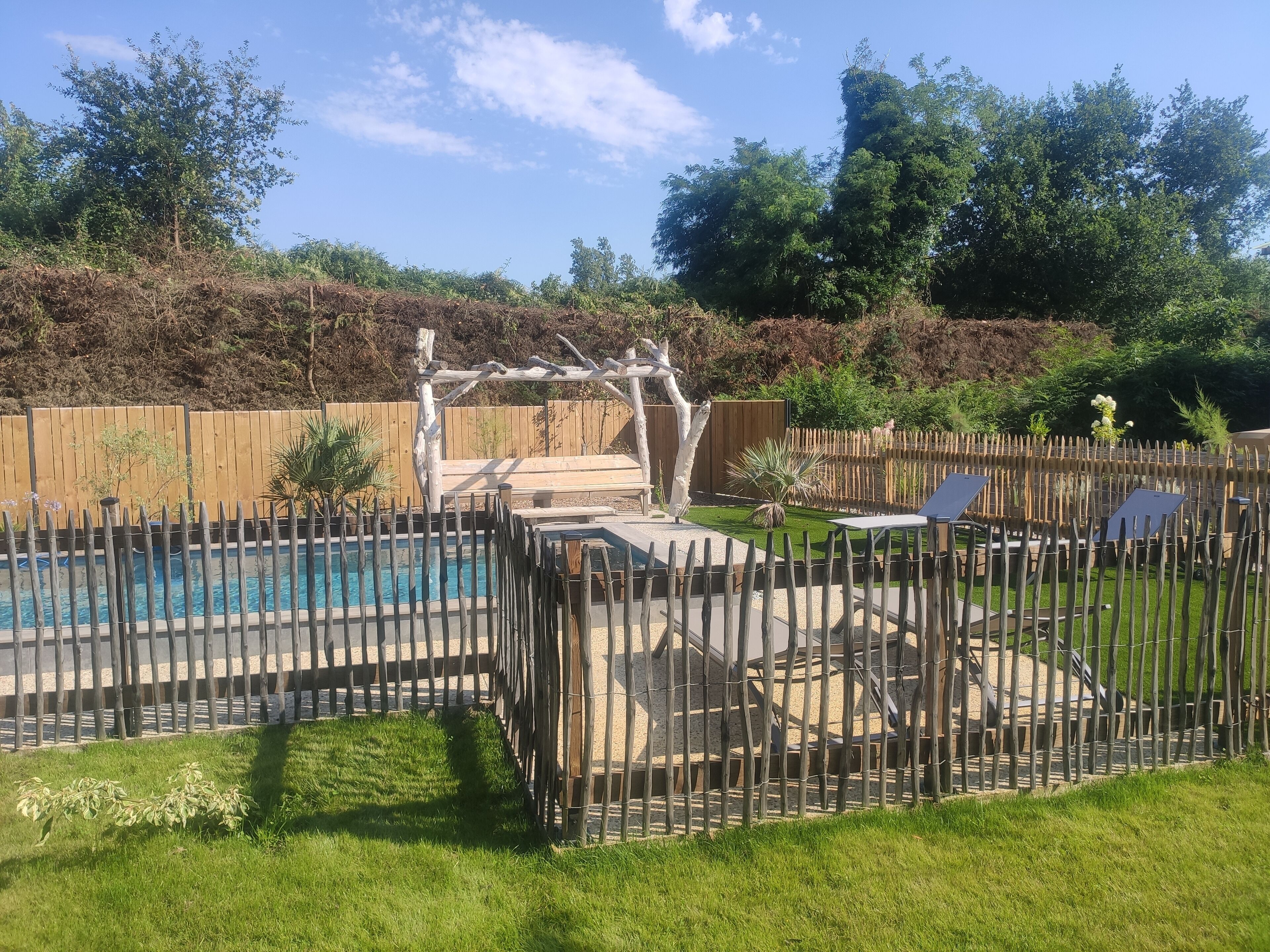 A backyard with a swimming pool, wooden deck, and a fenced area with lounge chairs.