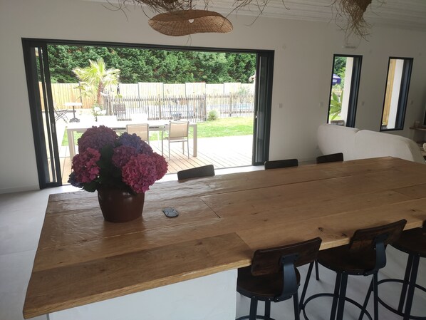 A spacious room with a large wooden table, a potted plant, and a view of an outdoor patio area. - Nouveau !! Villa Matiou (Linxe)