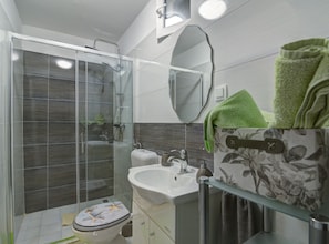 Un baño moderno con ducha envuelta en vidrio, un lavamanos blanco y un inodoro con diseño de estrella de mar.