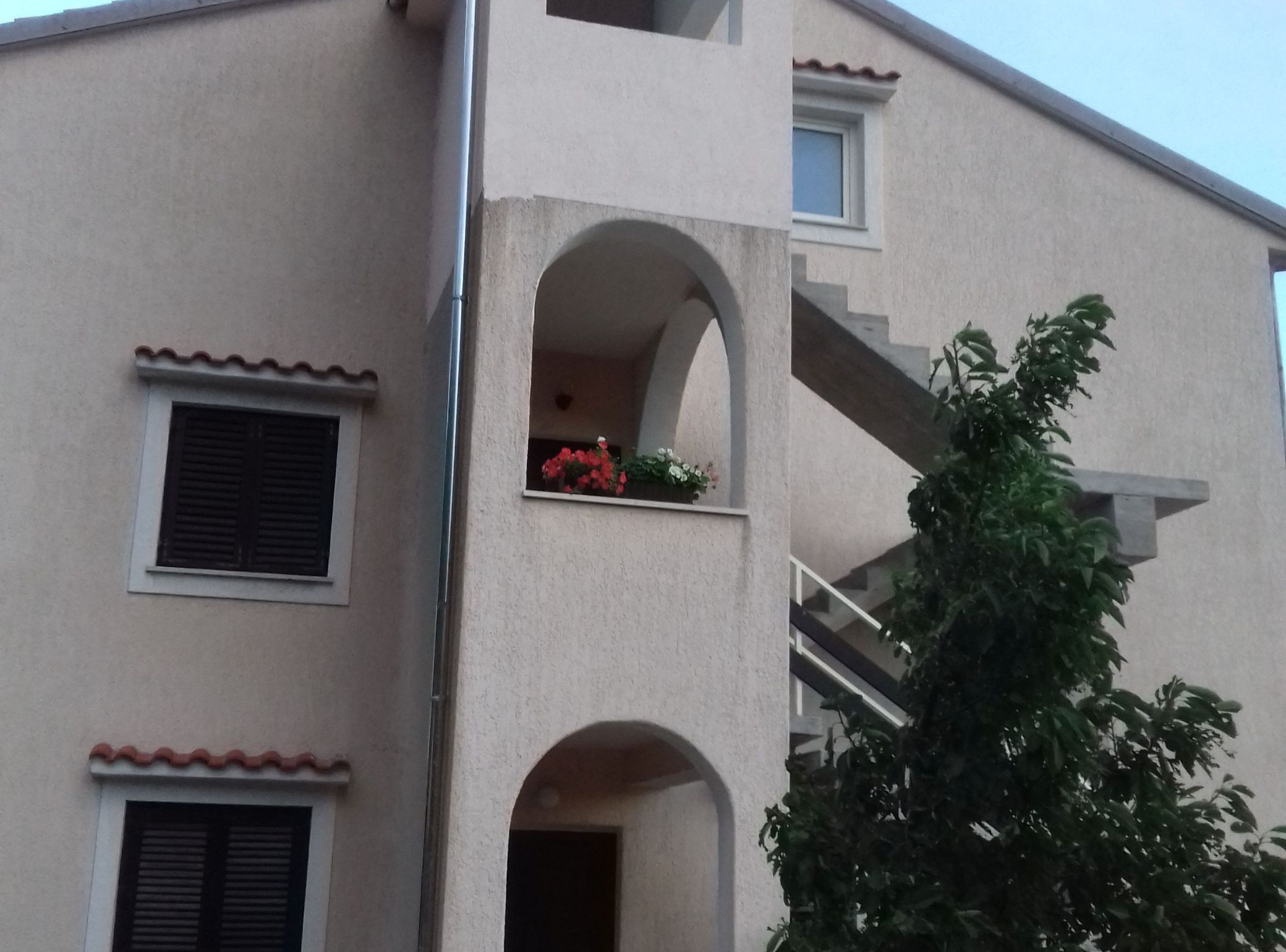 A multi-story building with balconies, a staircase, and a window with flowers.