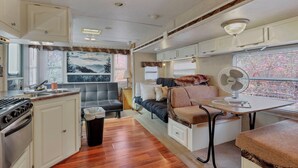 A compact RV interior with a kitchenette, a seating area with a sofa and table, and a window with a view. - Big spacious Camper (New Lexington)