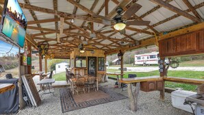 A covered outdoor seating area with wooden tables and chairs, a TV screen, and a grill. - Big spacious Camper (New Lexington)