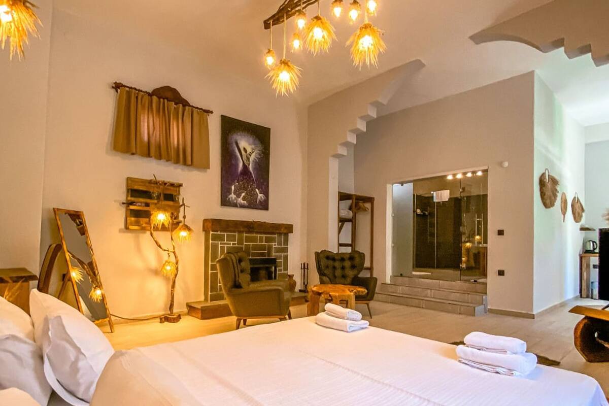 A spacious bedroom with a large bed, a fireplace, and a view of a glass-enclosed bathroom.