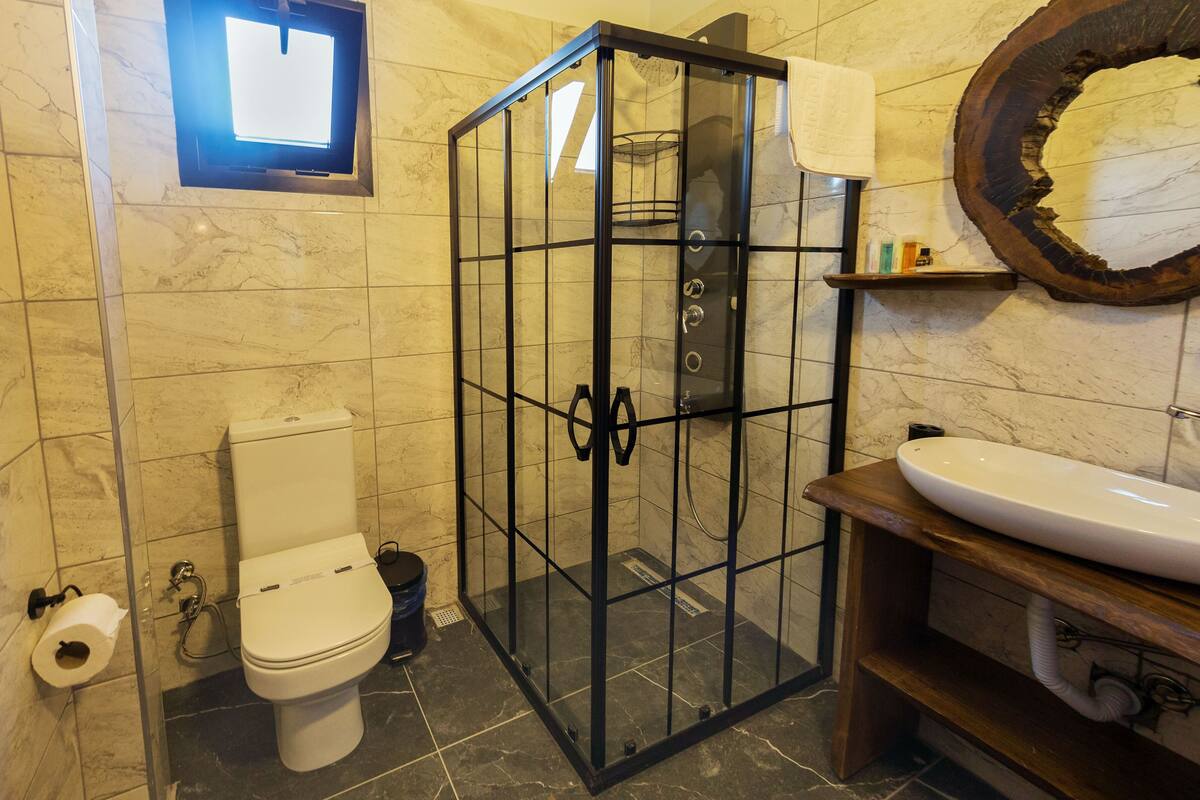 A bathroom with a glass-enclosed shower, a toilet, a sink, and a mirror with a unique design.