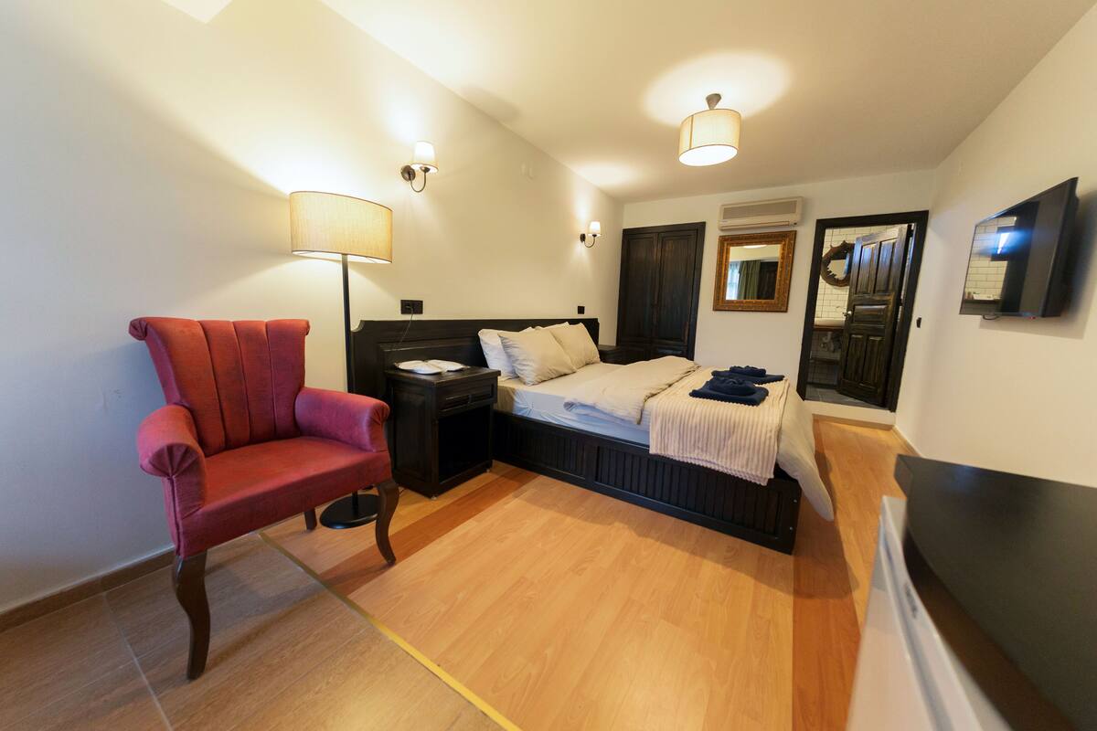 A bedroom with a bed, bedside table, lamp, chair, and a TV mounted on the wall.