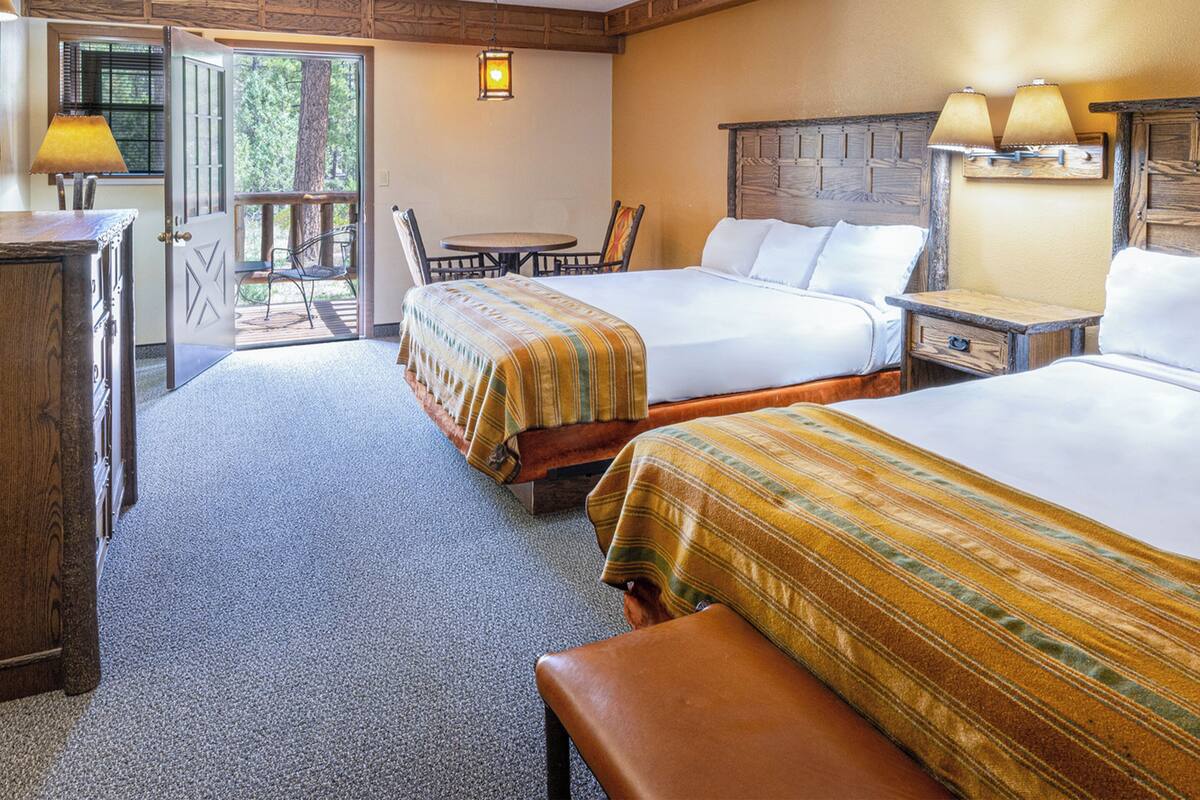 A hotel room with two beds, a wooden headboard, a small table, and a chair.