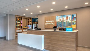 A hotel reception area with a modern design, including a reception desk, a 'Welcome to Hampton' sign, a cityscape artwork, and a 'Hilton Honors' sign. - Hampton Inn & Suites Little Rock Airport (Little Rock)