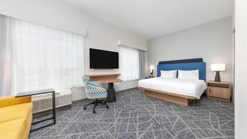 A hotel room with a bed, a desk, a chair, a TV, and a lamp.