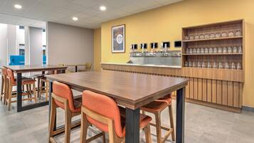 Un café moderno con mesas y sillas de madera, una barra con máquina de café y un estante con vasos.