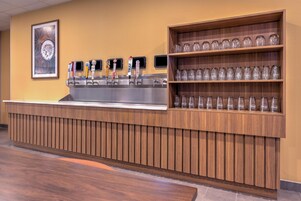 Una zona de bar con varias grifos, una barra de madera y estantes con copas.
