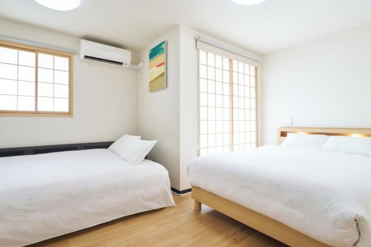 A hotel room with two beds, a window, an air conditioning unit, and a wall-mounted artwork.