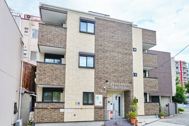 Un immeuble résidentiel à plusieurs étages, sur lequel on peut lire l’inscription « Miyoshi House ».