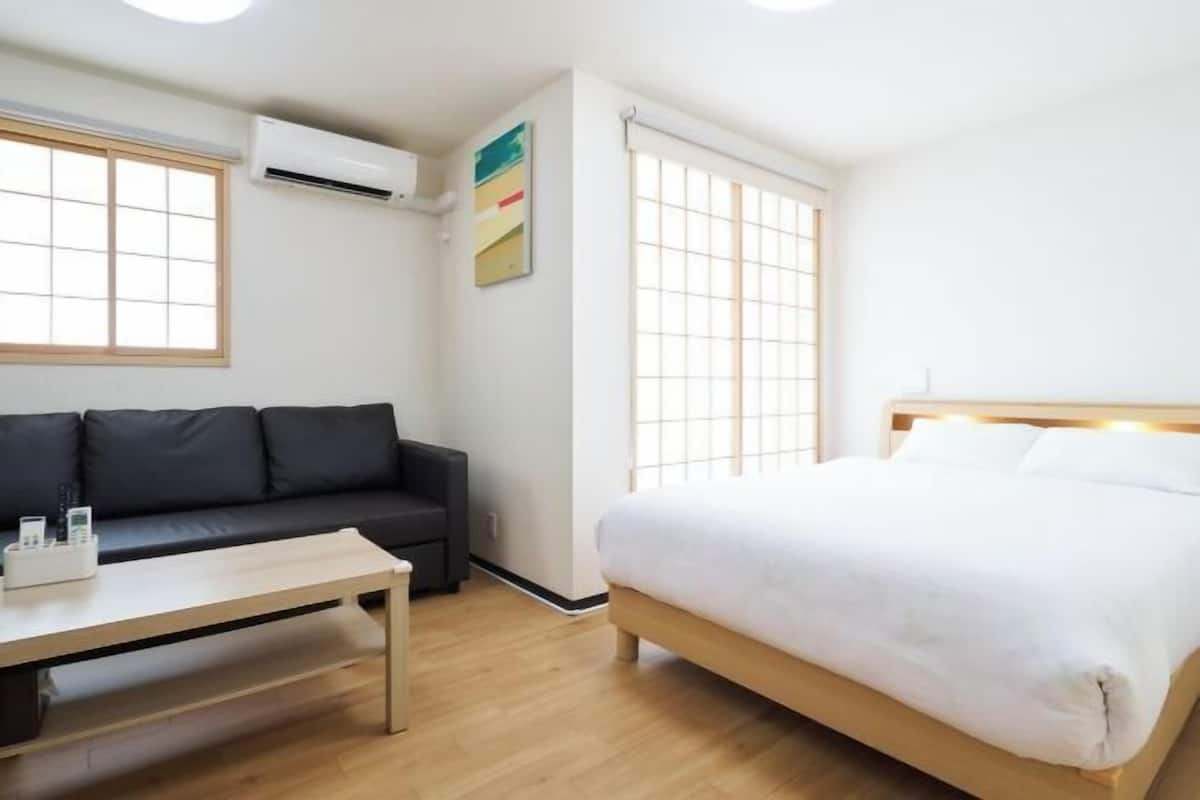 A modern hotel room with a bed, a sofa, a table, and a window.