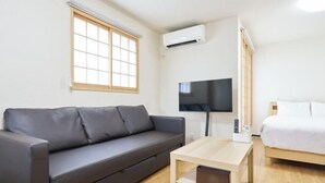 A modern room with a grey sofa, a wooden coffee table, a bed with white bedding, a TV mounted on the wall, and an air conditioning unit. - Miyoshi House Nonsmoking Self Checkin (Osaka)