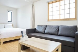 A room with a bed, a grey sofa, a wooden coffee table, and a window with blinds. - Miyoshi House Nonsmoking Self Checkin (Osaka)