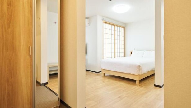 A bedroom with a bed, a wooden floor, a window with a grid pattern, and a door. - Miyoshi House Nonsmoking Self Checkin (Osaka)
