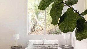 A bedroom with a large bed, a hanging plant, a window with a view of trees, and a modern chandelier. - Treehouse studio, secluded & chic hiker’s paradise

 (San Anselmo)