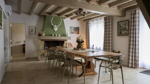 A dining area with a long wooden table and metal chairs, a fireplace, and a view of the outdoors through large windows.