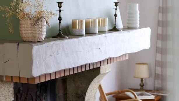 A fireplace with a stone mantle, a deer antler decoration, and a basket of dried flowers.