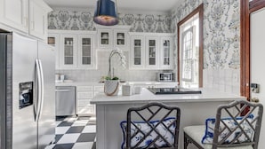 A modern kitchen with white cabinetry, a central island with chairs, a refrigerator, and a microwave. - Home in East End Historic Galveston, Coco Shores (Galveston)